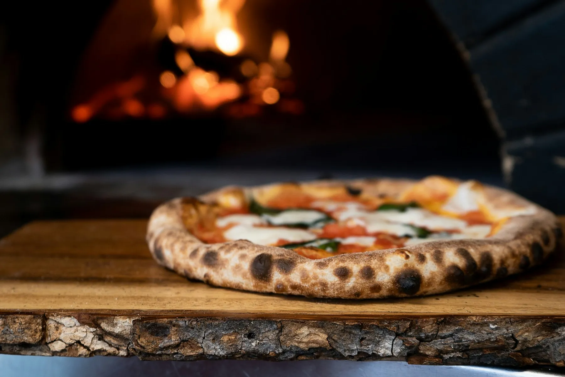 Una pizza margherita davanti al forno a legna acceso
